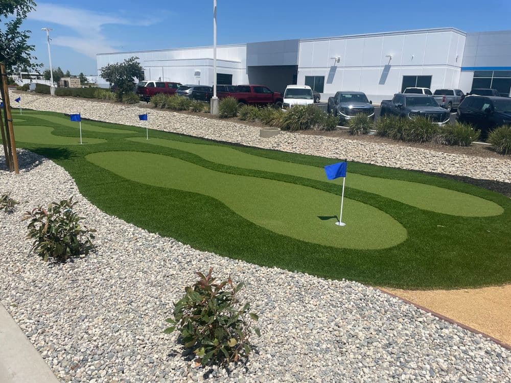 Putting green with blue flags and landscaped gravel area in a corporate environment.