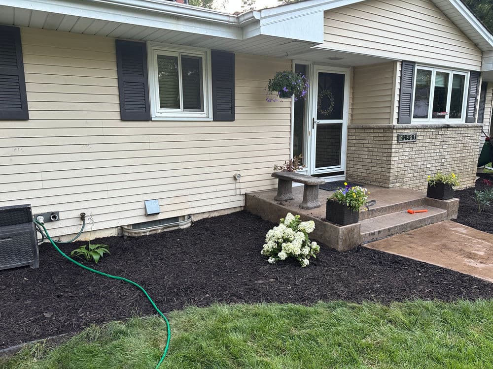 Front yard of a home with landscaped garden, flowers, and patio entrance.