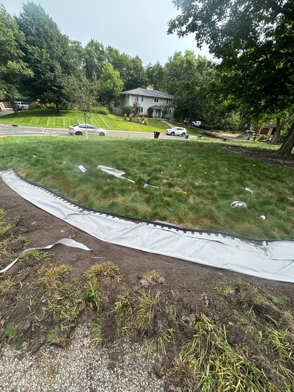 Installation of landscaping fabric on a residential lawn with surrounding greenery.