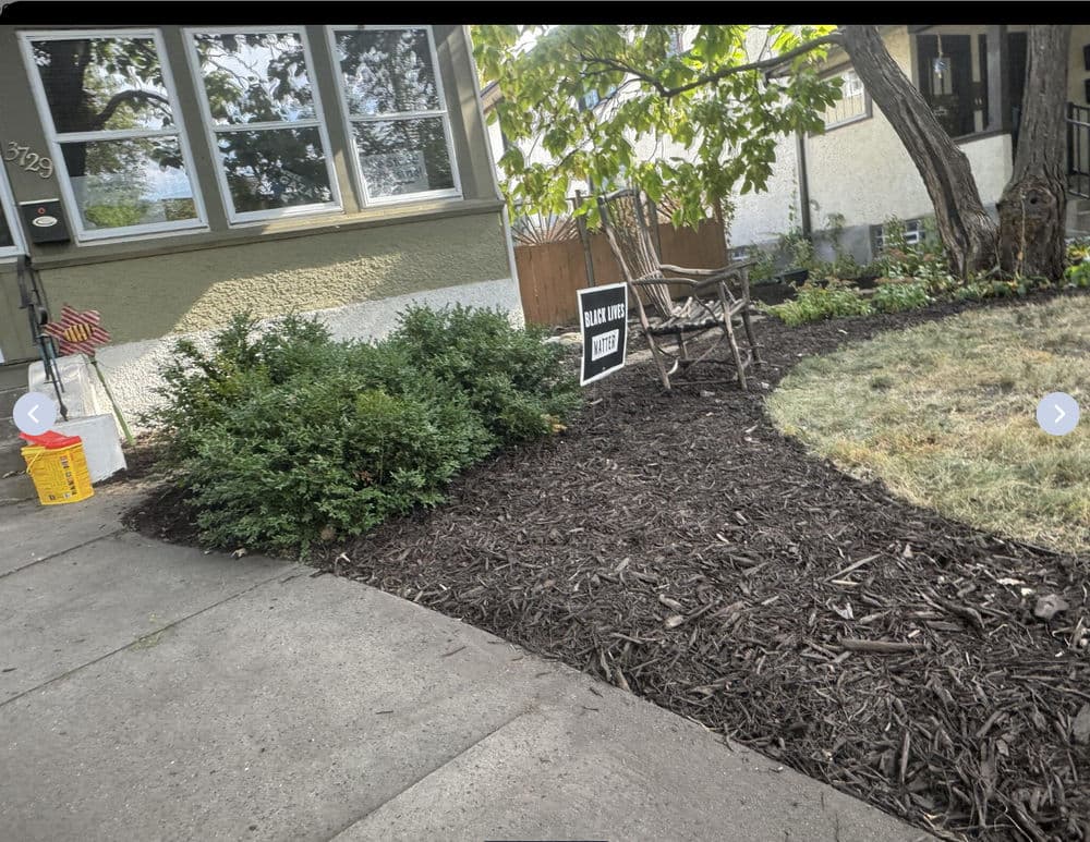 Mulched garden area with shrubs, chair, and house in background, promoting landscaping services.