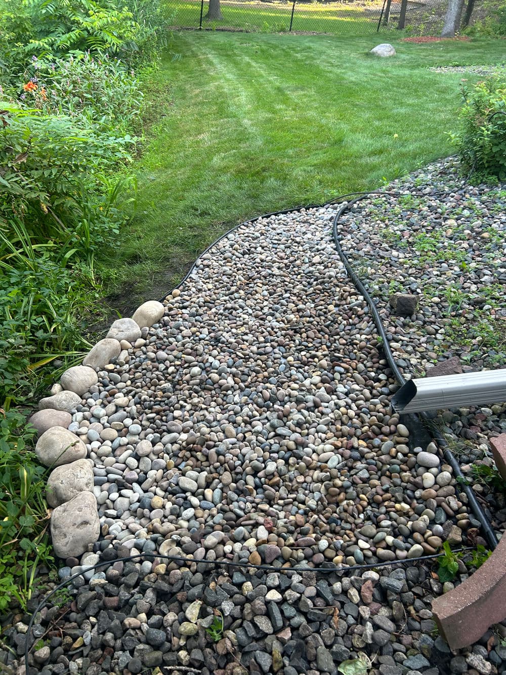 Pathway made of decorative stones and pebbles, bordered by greenery and lawn.