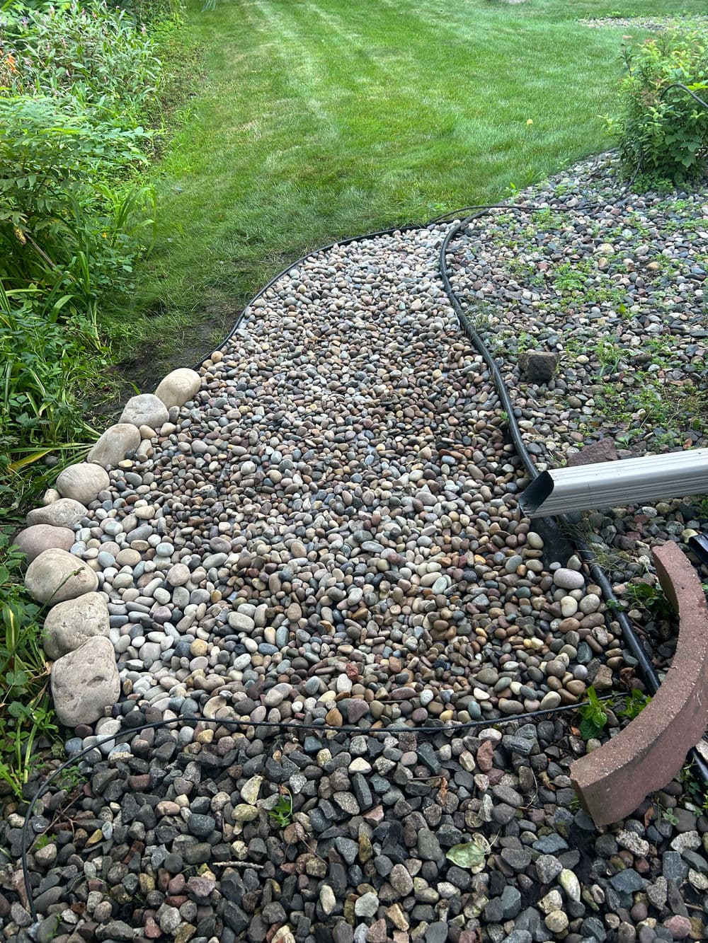 Gravel pathway bordered by river rocks in a green garden setting.