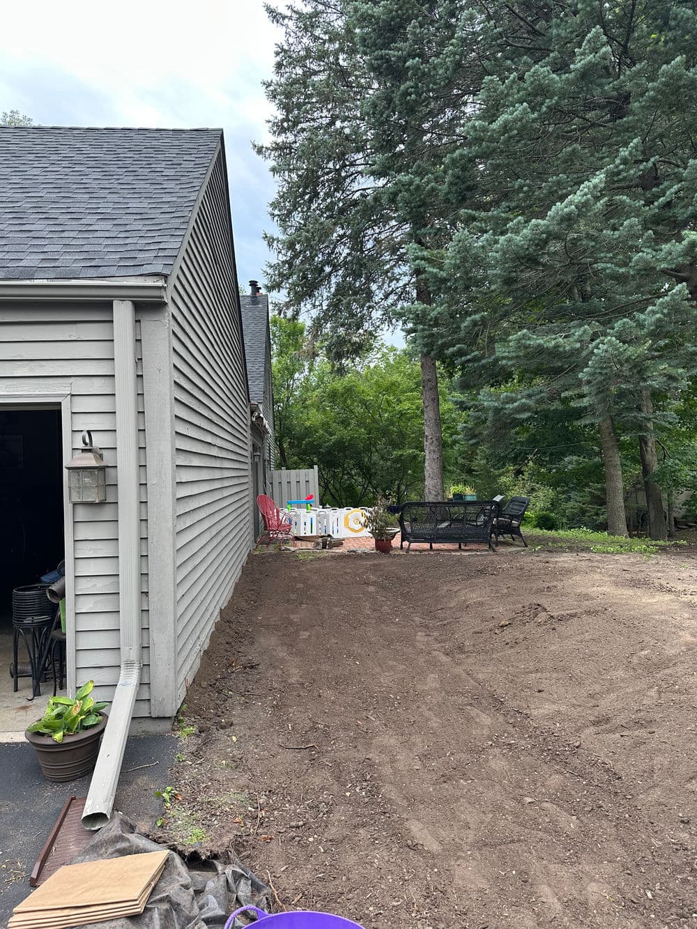 Backyard patio area with gravel and seating near house, surrounded by trees.