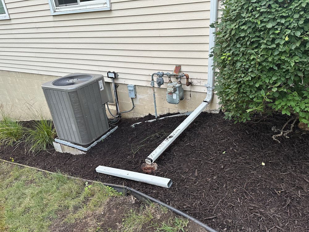 Air conditioning unit and gas meter installation beside a house with mulch landscaping.