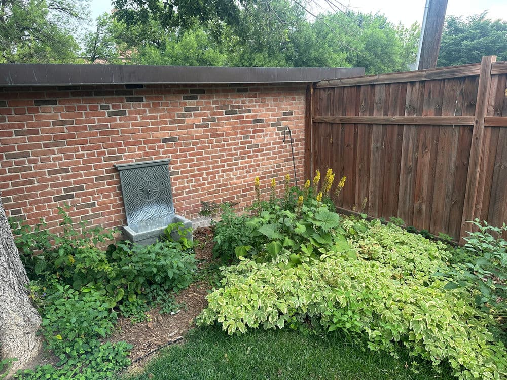 Garden area with brick wall, wooden fence, and greenery surrounding a stone water fountain.