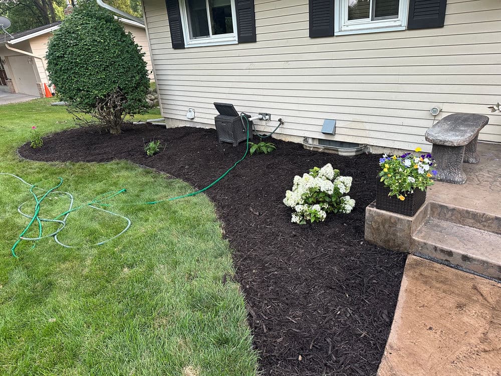 Landscaped yard featuring mulch, flowers, and outdoor seating by a house.