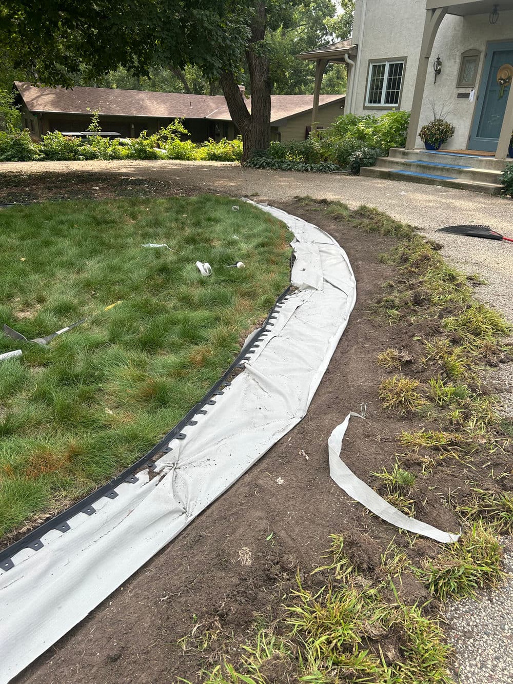 Lawn edging installation with fabric barrier and freshly disturbed soil alongside a house.
