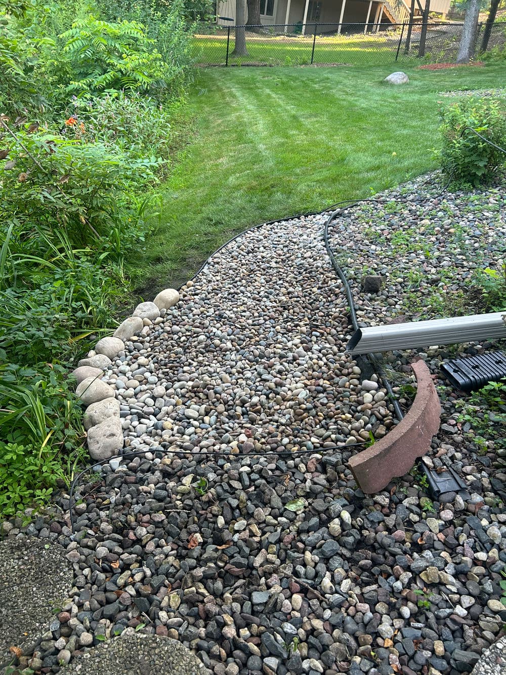 Garden pathway lined with stones, leading to a green lawn and lush shrubs.