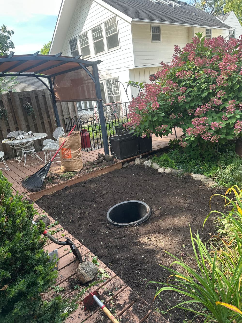Garden area preparation with a sunken pit, surrounded by blooming hydrangeas and patio furniture.