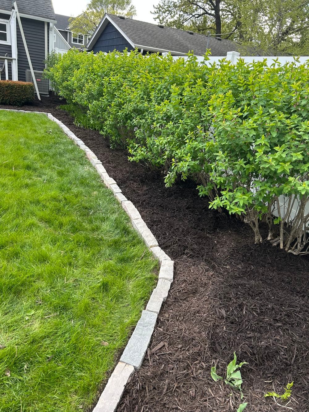 Lush green landscaping with a curved stone border and freshly mulched flower bed.